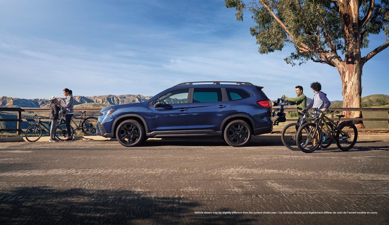 vue latérale d'une Subaru Outback 2024 sur le bord de la route près d'un groupe de cyclistes