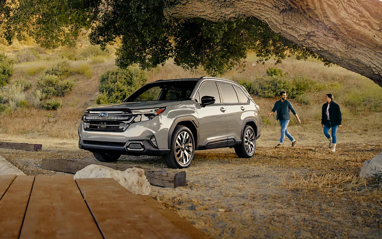 couple qui s'approchent d'une Subaru Forester 2025 sous un grand arbre en campagne 