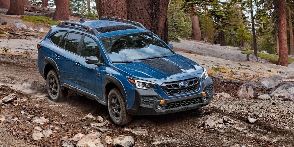 Vue trois quarts avant du Subaru Outback Wilderness 2025 bleu sur un sentier rocailleux en forêt, en pleine descente, soulignant ses capacités hors route.